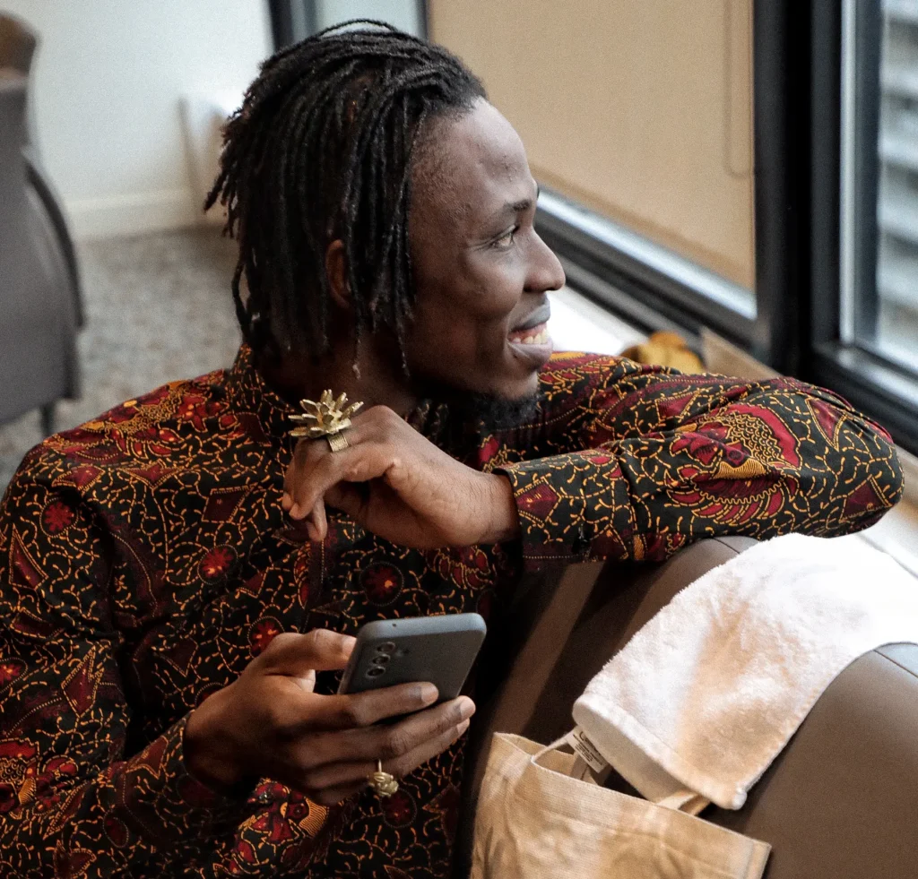 A person in a colourful shirt holds a phone in one hand and smiles out a window