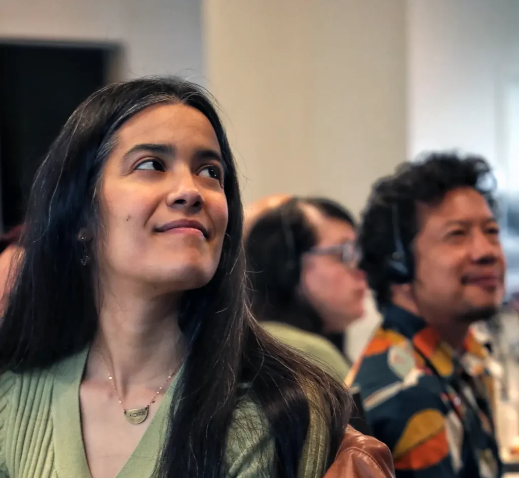 A person in a green sweater smiles from a conference table